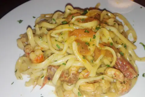 Un piatto invitante di tagliolini agli scampi, con pasta fresca e succulenti crostacei in una cremosa salsa, guarnito con prezzemolo tritato.