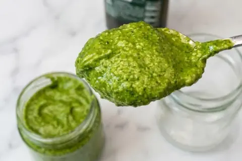 Un cucchiaio pieno di pesto fatto in casa, verde brillante, pronto per essere gustato.