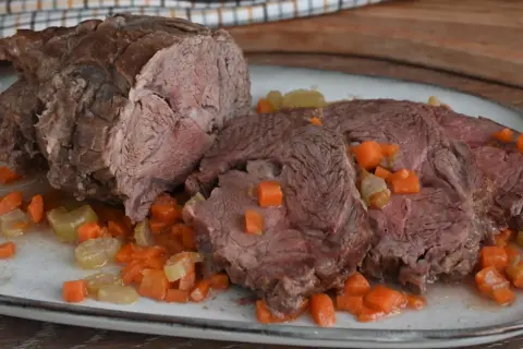 Arrosto di vitello morbido con sughetto e verdure. La carne è succulenta e tagliata a fette, immersa in un delizioso sughetto con carote e sedano a cubetti.