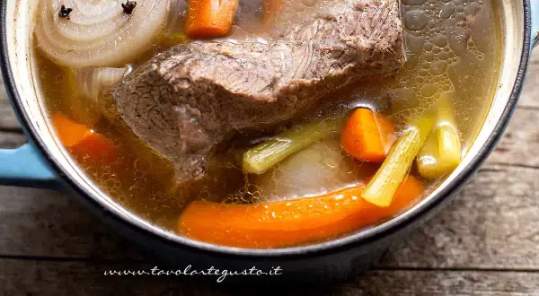 Brodo di carne ricetta: un pezzo di carne, carote, sedano e cipolla con chiodi di garofano bollono in una pentola.