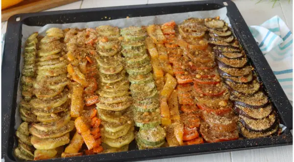 Vassoio con verdure al forno saporite disposte a raggiera: zucchine, carote, peperoni, pomodori e melanzane, condite con pangrattato.