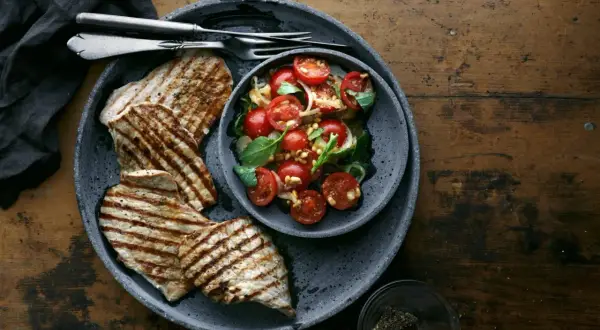 Delizioso paillard di vitello grigliato servito con un'insalata fresca di pomodorini, basilico e pinoli.