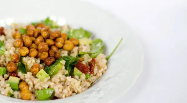 Un piatto di cous cous estivo con ceci croccanti, avocado, pomodori secchi e verdure fresche.