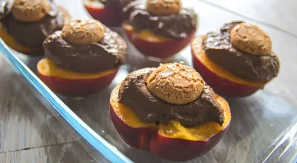 Pesche al forno con amaretti: dolci metà di pesche rosse ripiene di crema al cioccolato e guarnite con un amaretto croccante.