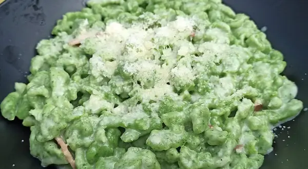 Spätzle alla tirolese verdi, conditi con panna e parmigiano, serviti in un piatto nero.