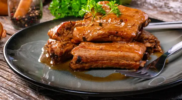 Succulente costine in umido, condite con erbe aromatiche e servite su un piatto scuro. Un piatto invitante e saporito.