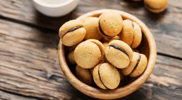 Baci di dama, deliziosi biscotti con ripieno di cioccolato, in una ciotola di legno su un tavolo rustico.