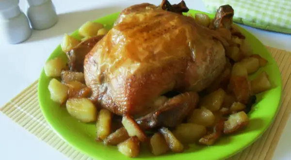 Un succulento pollo allo spiedo dorato, servito su un piatto verde brillante con patate arrosto.
