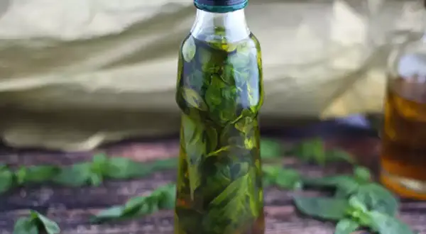 Olio al basilico fatto in casa da Benedetta, profumato e verde brillante, in una bottiglia su un tavolo di legno.