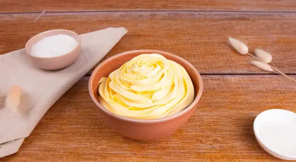 Una ciotola piena di soffice crema al burro, pronta per decorare torte. Accanto, ciotoline con zucchero e decorazioni naturali.