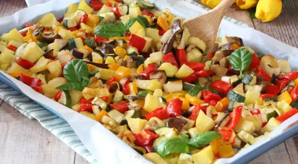 Un colorato mix di verdure in padella, con patate, peperoni, zucchine e melanzane, guarnito con basilico fresco.
