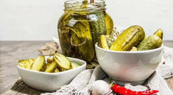 Cetrioli in agrodolce in un barattolo di vetro e in ciotole, con aglio e peperoncino.