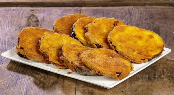 Fette di melanzane fritte solo con farina, dorate e croccanti, servite su un piatto bianco.
