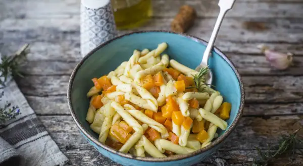 Piatto di pasta con un saporito ragù di verdure, zucca e rosmarino, servito in una ciotola blu su un tavolo di legno rustico.