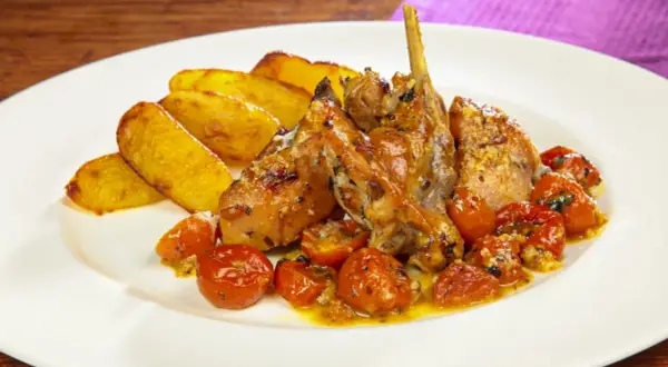 Delizioso coniglio al forno con patate arrosto e pomodorini confit, un piatto succulento e saporito.