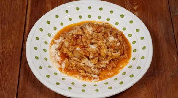 Un piatto di trippa alla fiorentina, ricca e saporita, cosparsa di parmigiano, servita su un piatto bianco decorato.