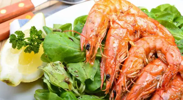 Gamberoni succulenti, pronti per la griglia, con un'insalata fresca e una fetta di limone. La marinatura per gamberoni alla griglia è il segreto del loro sapore.