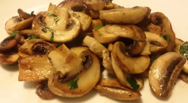 Funghi champignon in padella, dorati e succulenti, guarniti con prezzemolo fresco. Un contorno semplice e gustoso.