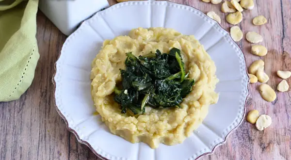 Piatto di fave e cicoria, un classico della cucina pugliese, servito su un piatto bianco con fave secche sparse attorno.