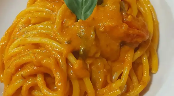 Un piatto invitante di pasta con i pomodorini, condita con una salsa cremosa e guarnita con una foglia di basilico fresco.