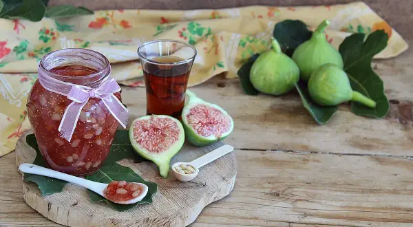 Un vasetto di marmellata di fichi, con fichi freschi, un bicchierino di liquore e un cucchiaino con la marmellata.