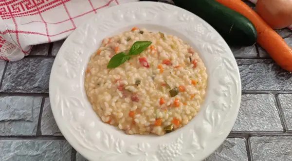 Un cremoso risotto con verdure, guarnito con basilico fresco. Accanto, carote, zucchine e cipolla, ingredienti per un piatto gustoso.