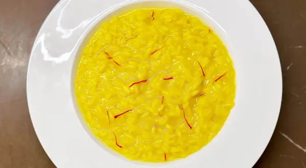 Un cremoso risotto alla milanese, giallo intenso con fili di zafferano, servito in un piatto bianco.