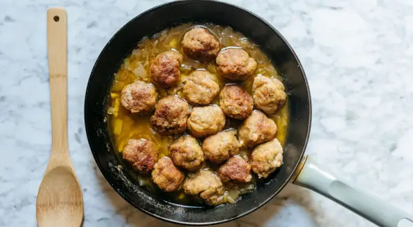 Polpette in bianco cremose in padella, dorate e succulente, pronte per essere gustate con un cucchiaio di legno.