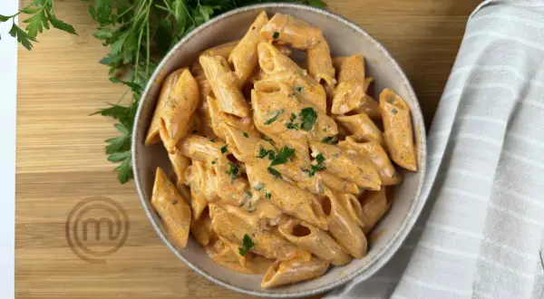Penne alla vodka cremose e invitanti, guarnite con prezzemolo fresco, su un tagliere di legno con il logo MasterChef.