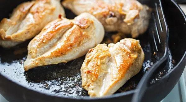 Petto di pollo dorato e succulento che sfrigola in padella, pronto per essere gustato.
