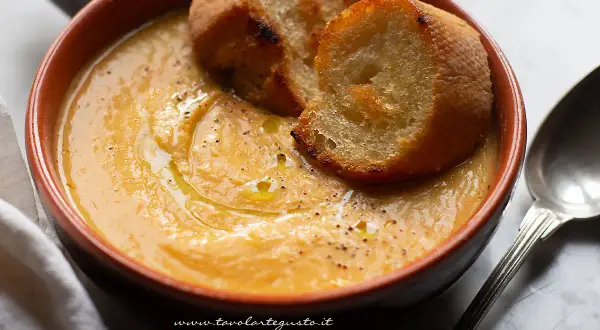 Una ciotola di terracotta con una cremosa zuppa di fagioli, guarnita con crostini dorati e un filo d'olio.