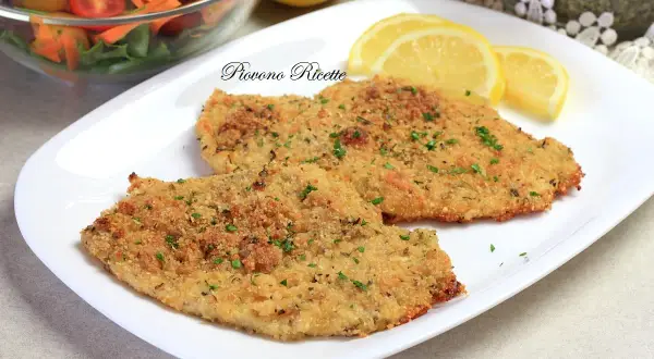 Due cotolette di pollo al forno dorate e croccanti, guarnite con prezzemolo fresco e servite con spicchi di limone e un'insalata mista.
