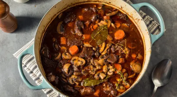 Un invitante spezzatino con funghi, carote e erbe aromatiche in una casseruola blu.