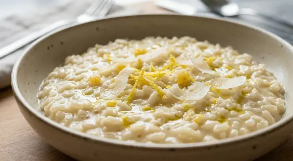 Cremoso risotto al limone, guarnito con scorza di limone e scaglie di parmigiano, pronto per essere gustato.
