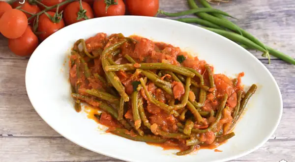Fagiolini in umido, un piatto saporito con fagiolini verdi cotti in un sugo di pomodoro e cipolla, accompagnato da pomodorini freschi.