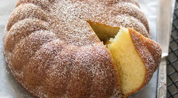 Torta 7 vasetti soffice e dorata, cosparsa di zucchero a velo. Una fetta è stata tagliata, rivelando l'interno profumato.