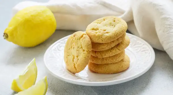 Biscotti senza burro al limone, dorati e fragranti, su un piatto bianco, con limoni freschi a lato.