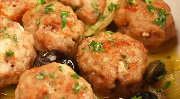 Polpette di carne succulente, dorate e profumate, servite con olive nere e un contorno di verdure.