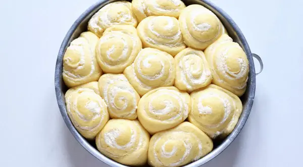 Torta di rose lievitata, pronta per essere infornata, con soffici spirali di pasta e una spolverata di zucchero a velo.