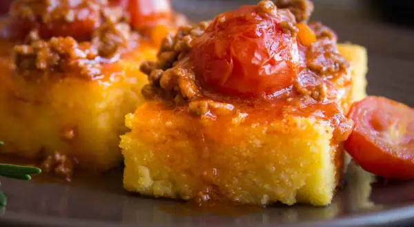 Polenta morbida ricoperta da un ricco sugo con salsiccia e pomodorini. Un piatto confortante e saporito.