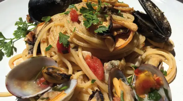 Spaghetti con cozze e vongole, un piatto cremoso e saporito, guarnito con prezzemolo fresco e pomodorini.
