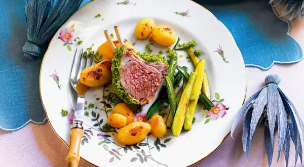 Carrè di agnello croccante con patate novelle e zucchine, un piatto elegante su un piatto fiorito.