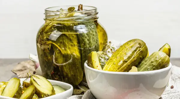Vaso di cetriolini in agrodolce, con alcuni in una ciotola. Profumo di aneto e spezie.