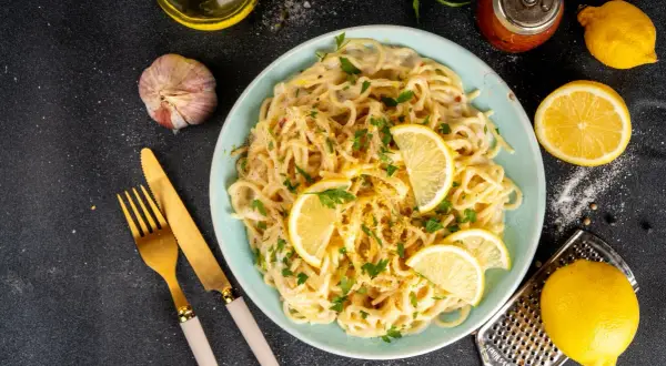 Spaghetti cremosi con un profumo agrumato, guarniti con spicchi di limone fresco e prezzemolo. Un piatto di pesto al limone che invita a gustare la freschezza.