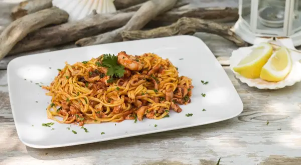 Un piatto di linguine al ragù di pesce, con gamberi e calamari, guarnito con prezzemolo e spicchi di limone su una conchiglia.