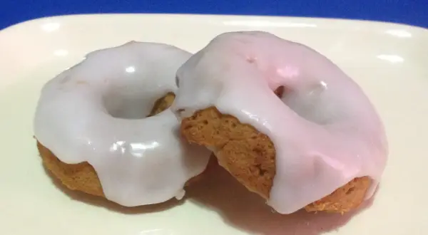 Due ciambelle con glassa per biscotti che si asciuga subito, su un piatto bianco.