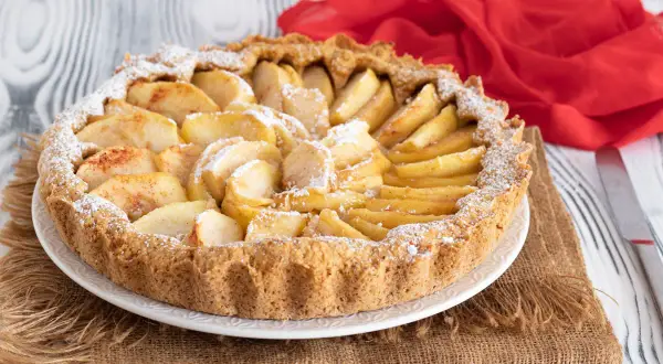 Una crostata di mele semplicissima, con mele a fette disposte a raggiera sulla base dorata, spolverata di zucchero a velo.