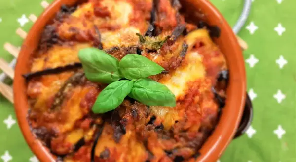 Deliziosa pasta alla norma al forno, con melanzane, pomodoro e basilico fresco, servita in una terrina di terracotta.