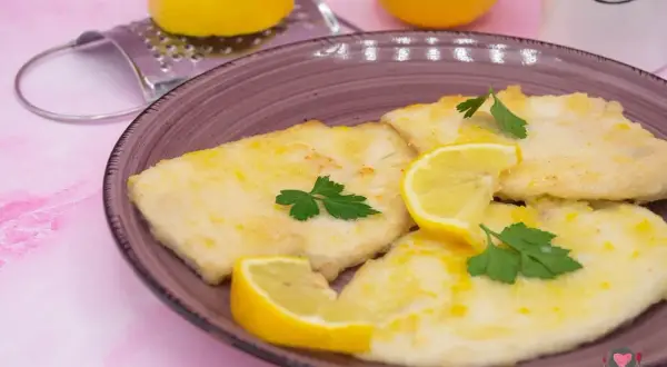 Deliziose scaloppine al limone, dorate e profumate, guarnite con spicchi di limone fresco e prezzemolo.