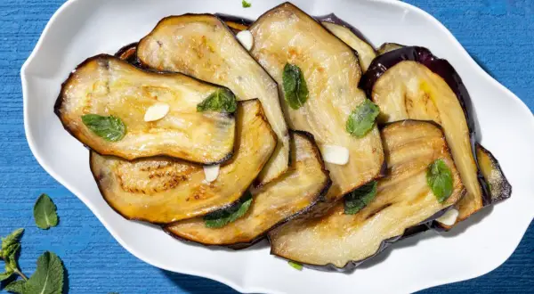 Fette di melanzane grigliate, guarnite con menta fresca e aglio, un contorno di verdure saporito e colorato.